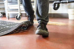 Trips, slips and falls in commercial kitchens are a major contributor to injuries sustained in the workplace. A food service worker tripping on a curled up floor mat.