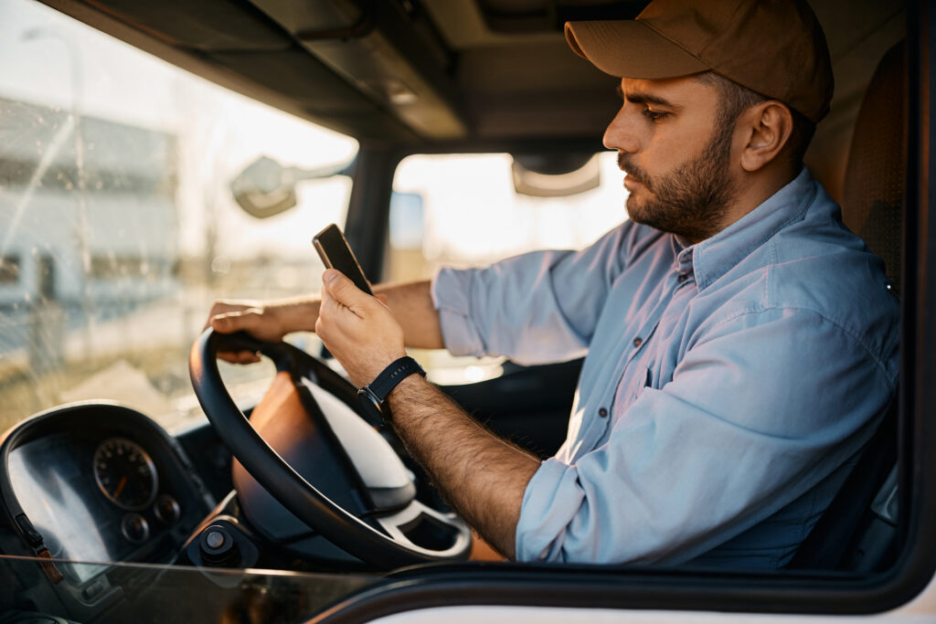 Young truck driver using mobile phone while driving transport vehicle.