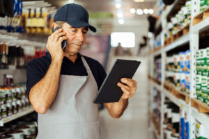 Elderly man working in a hardware store using a digital tablet while making a phone call. Small business concept.